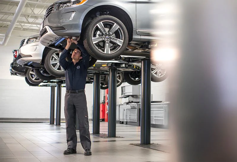 Volvo Service Technician looking at underneath of vehicle on a lift